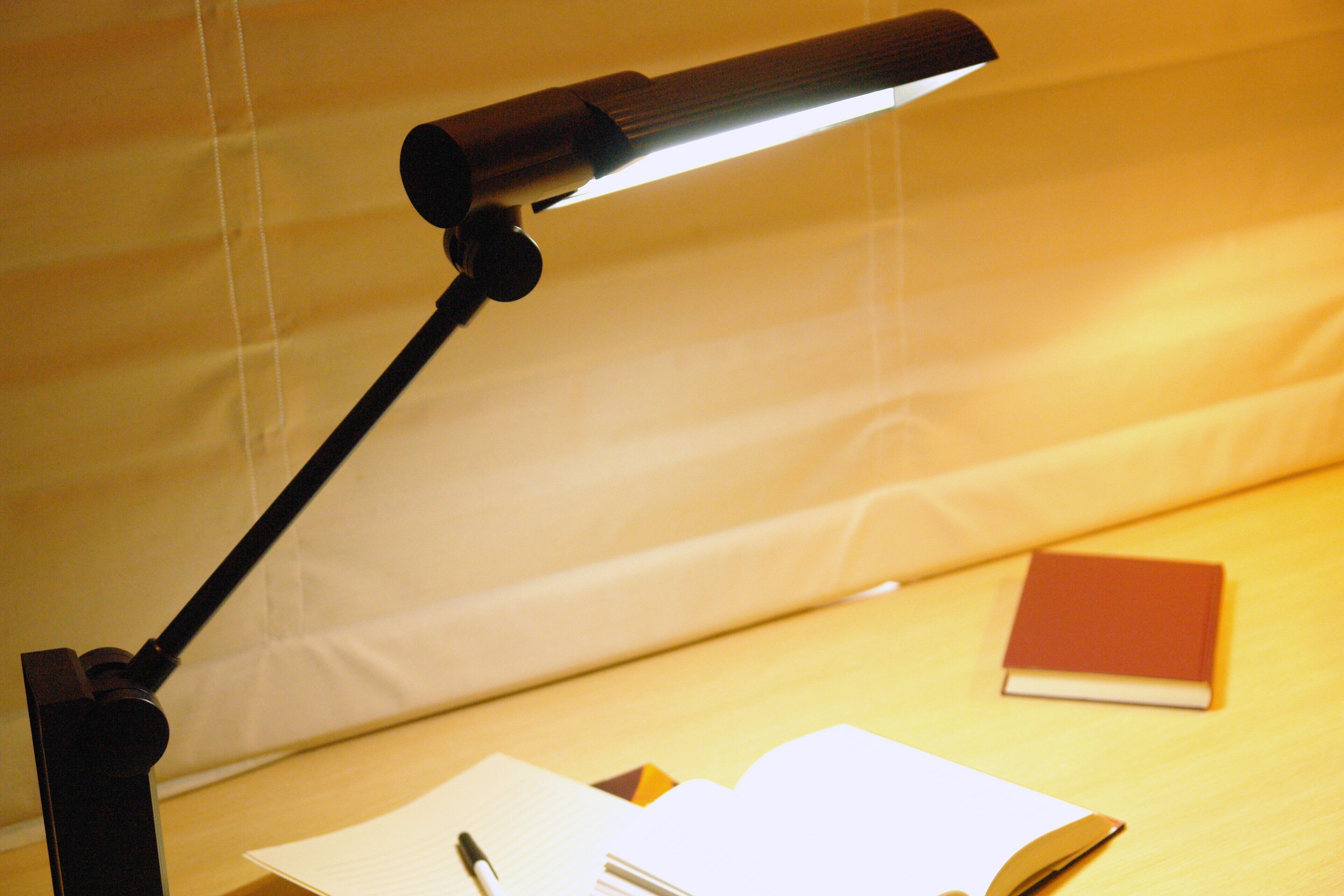 A desk with a desk lamp, an open notebook, and a closed book.
