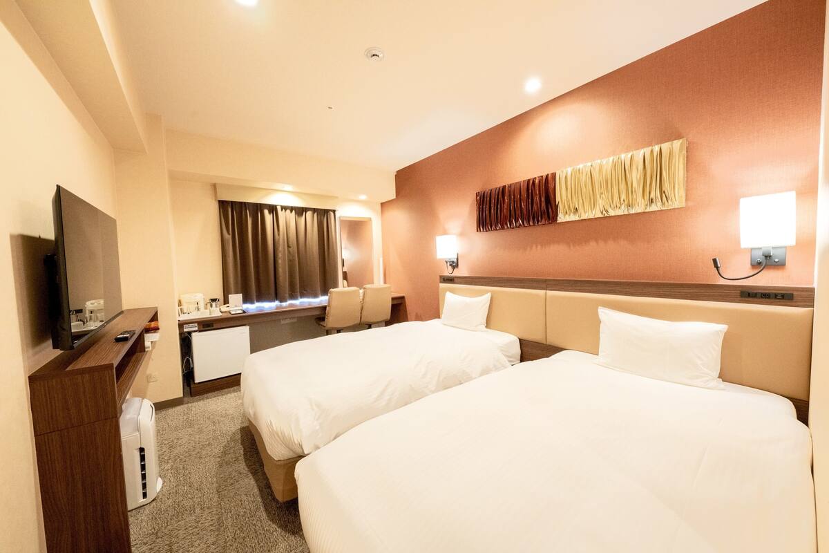 A hotel room with two beds, a desk, a TV, and a bathroom.