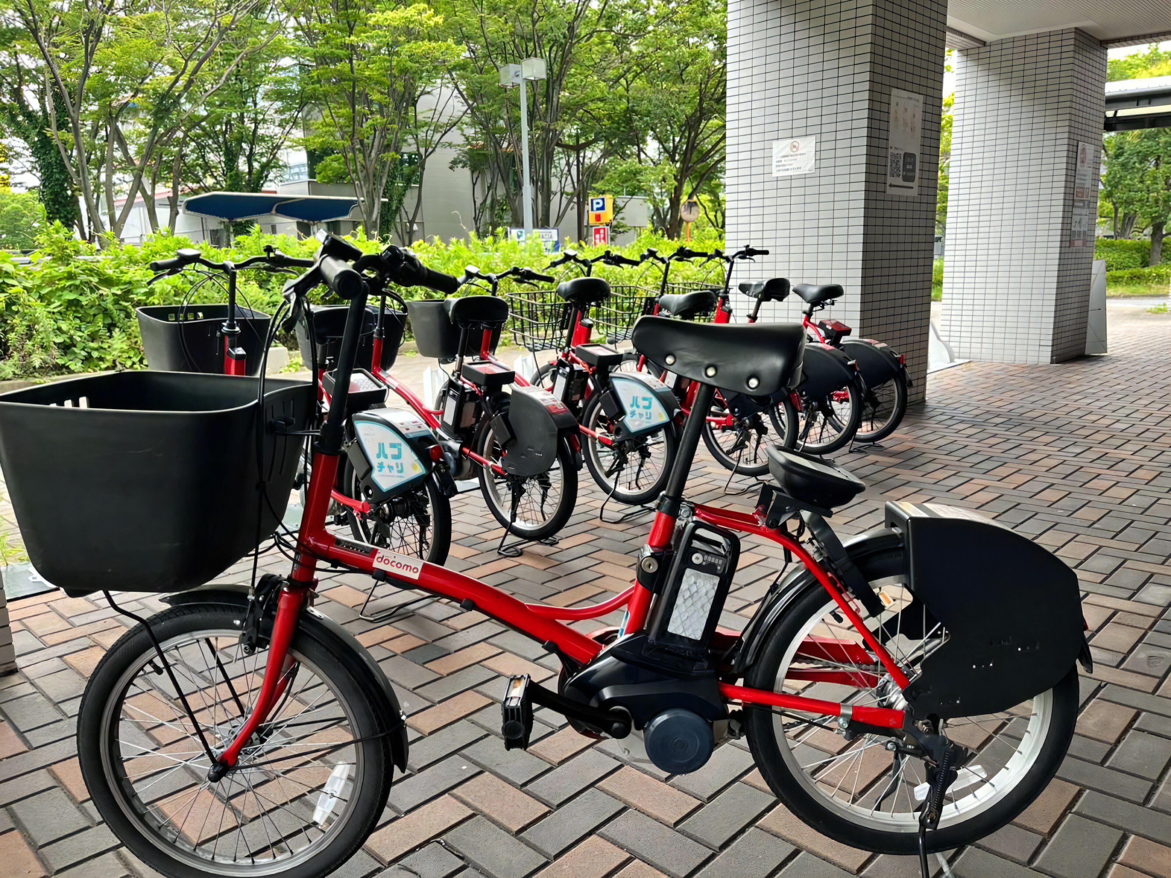 Una bicicleta roja con canasta negra y portaequipajes trasero, estacionada sobre adoquines.