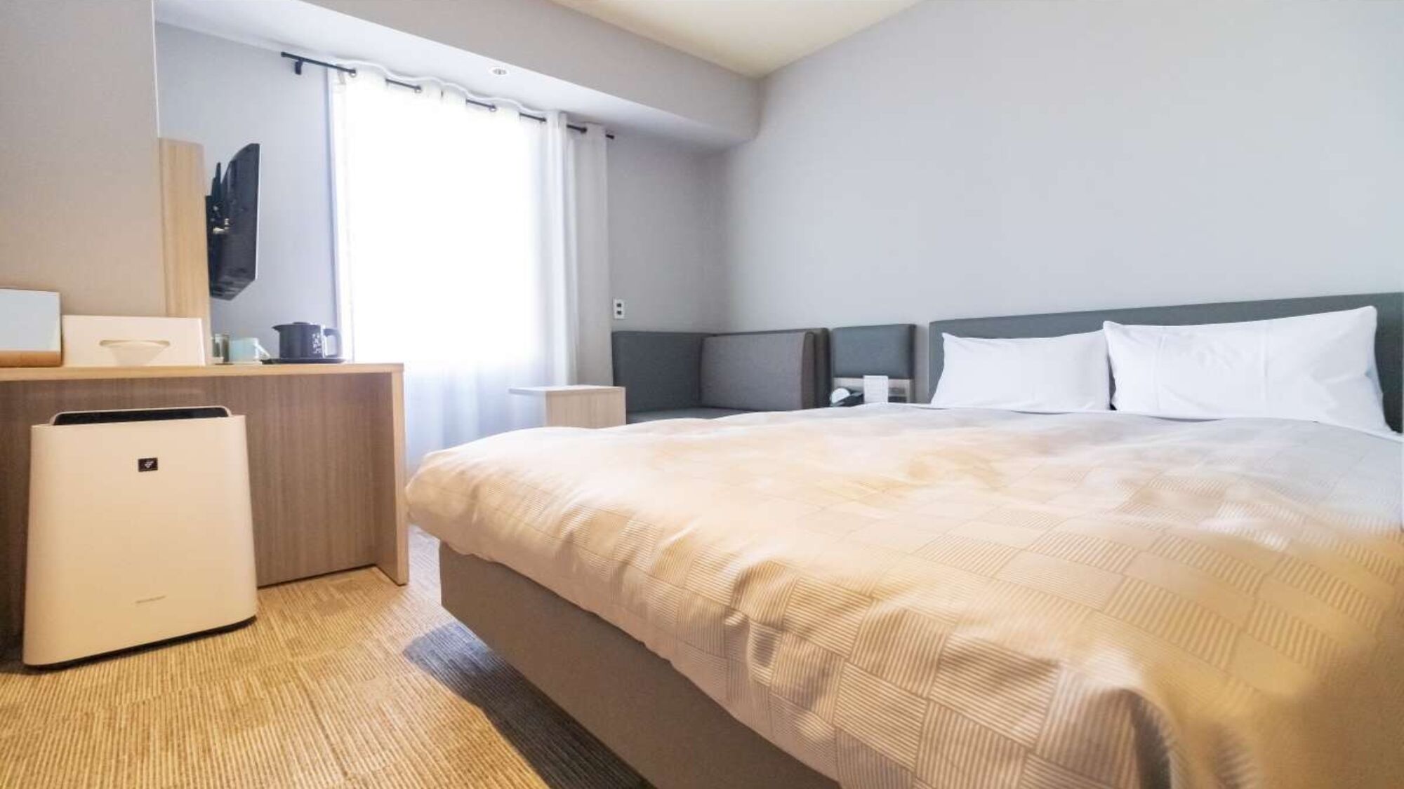 Een hotelkamer met een bed, een bureau, een stoel, een klein tafeltje, een televisie en een raam met gordijnen.