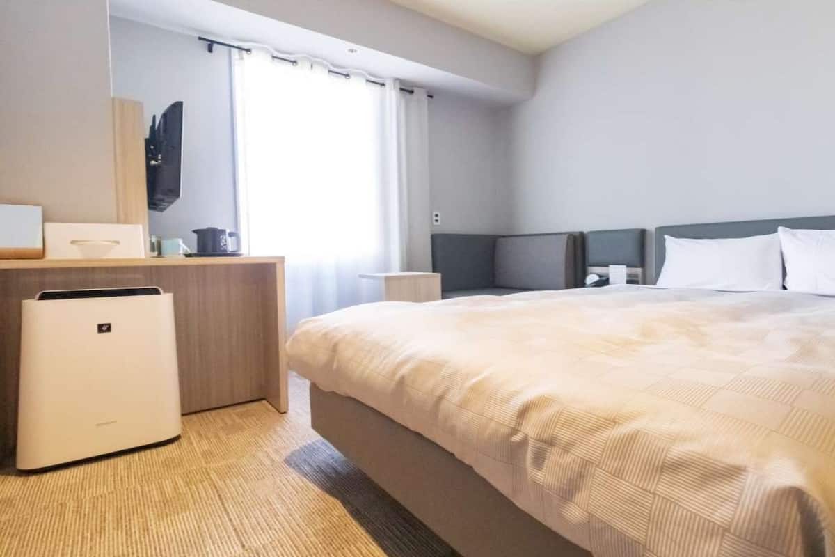 A hotel room with a bed, a desk, a chair, a small table, a television, and a window with curtains.