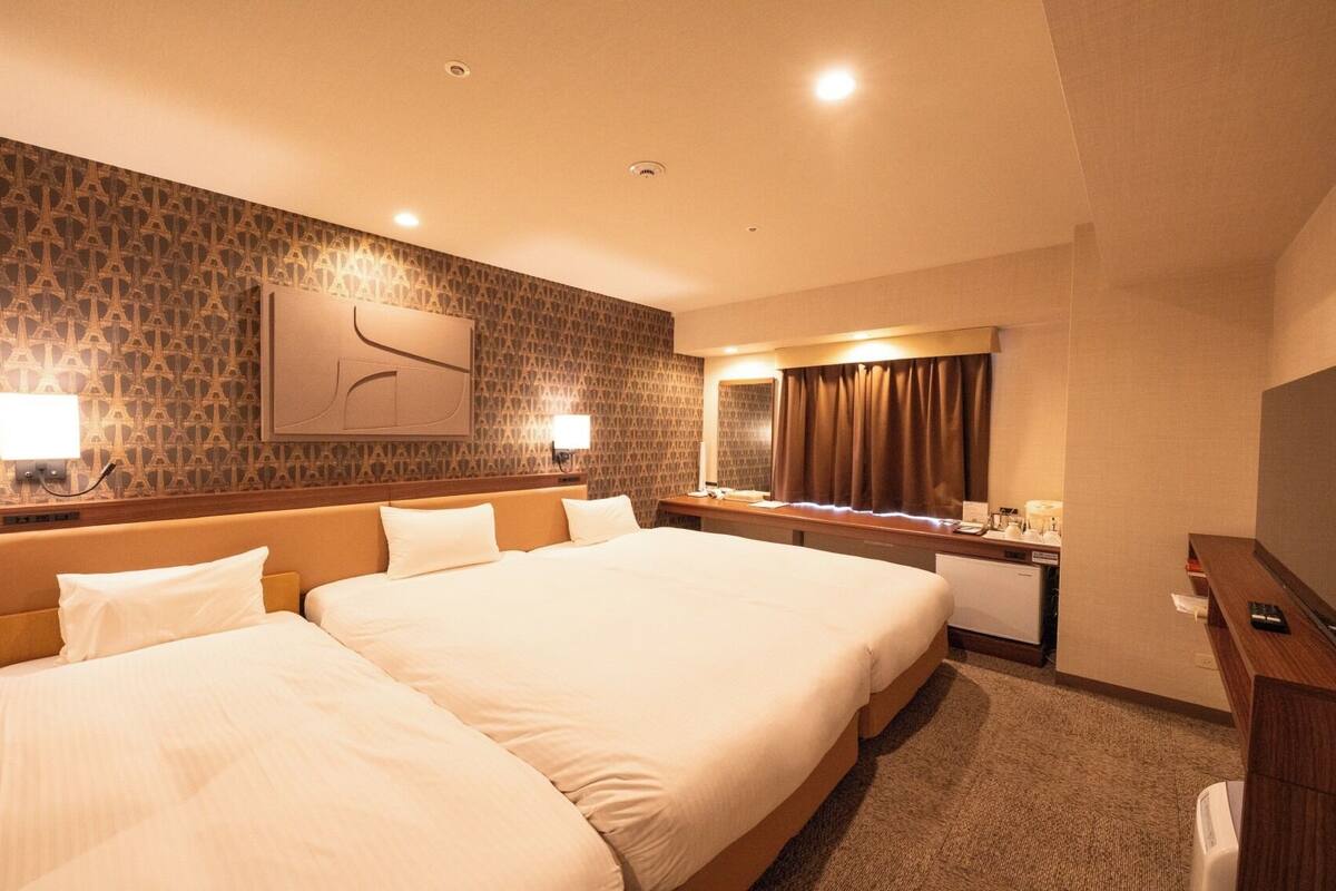 A hotel room with two beds, a desk, a TV, and a bathroom.