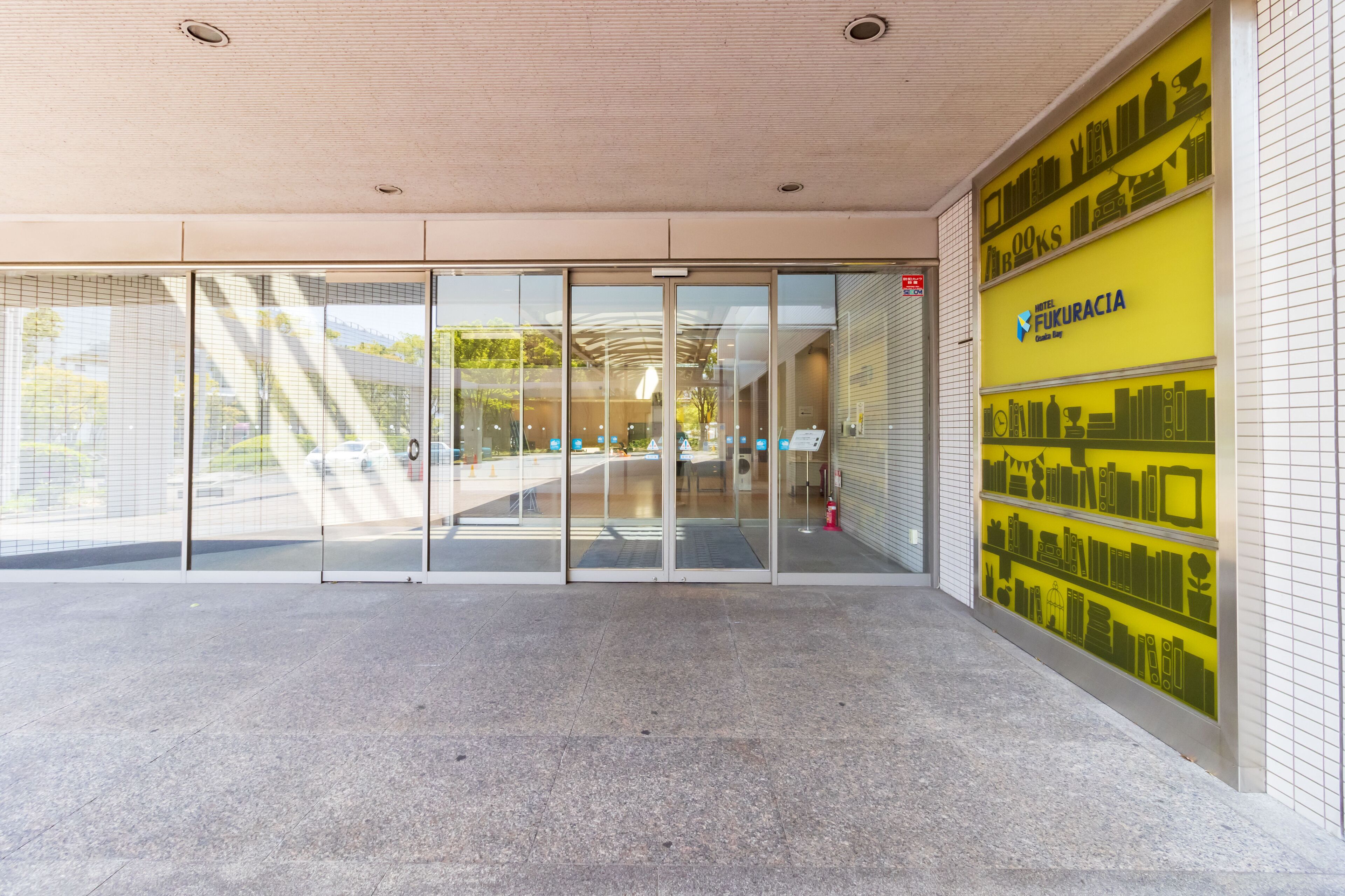 A building entrance with glass doors, a tiled floor, and a yellow wall with book icons.