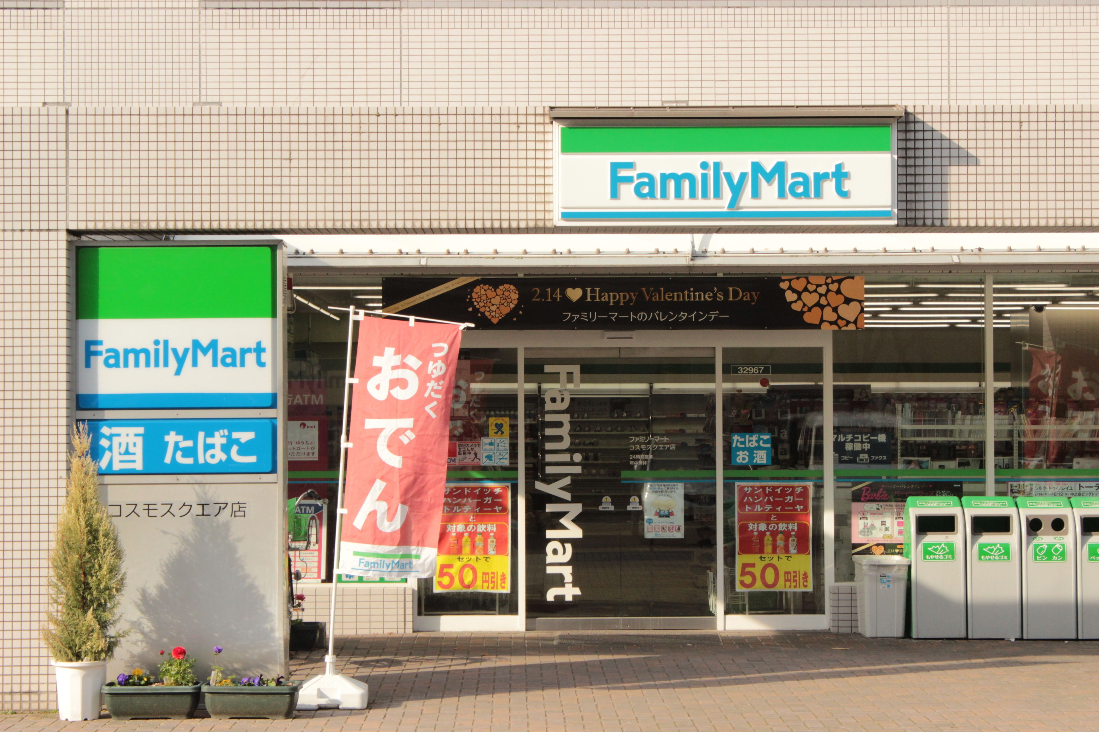 A FamilyMart store with a large sign, a Valentine's Day banner, and recycling bins outside.