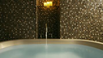Una bañera con un muro de mosaicos y una lámpara fijada a la pared.