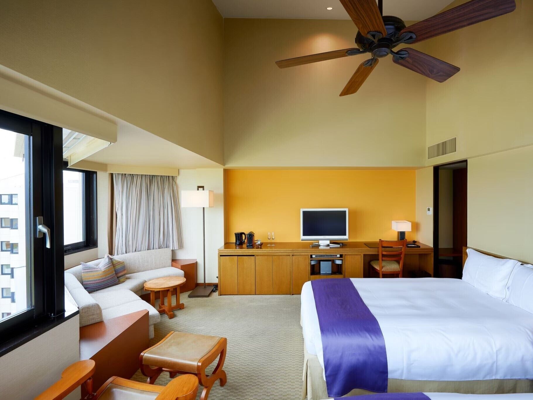A hotel room with a bed, a desk, a TV, a ceiling fan, and a window.
