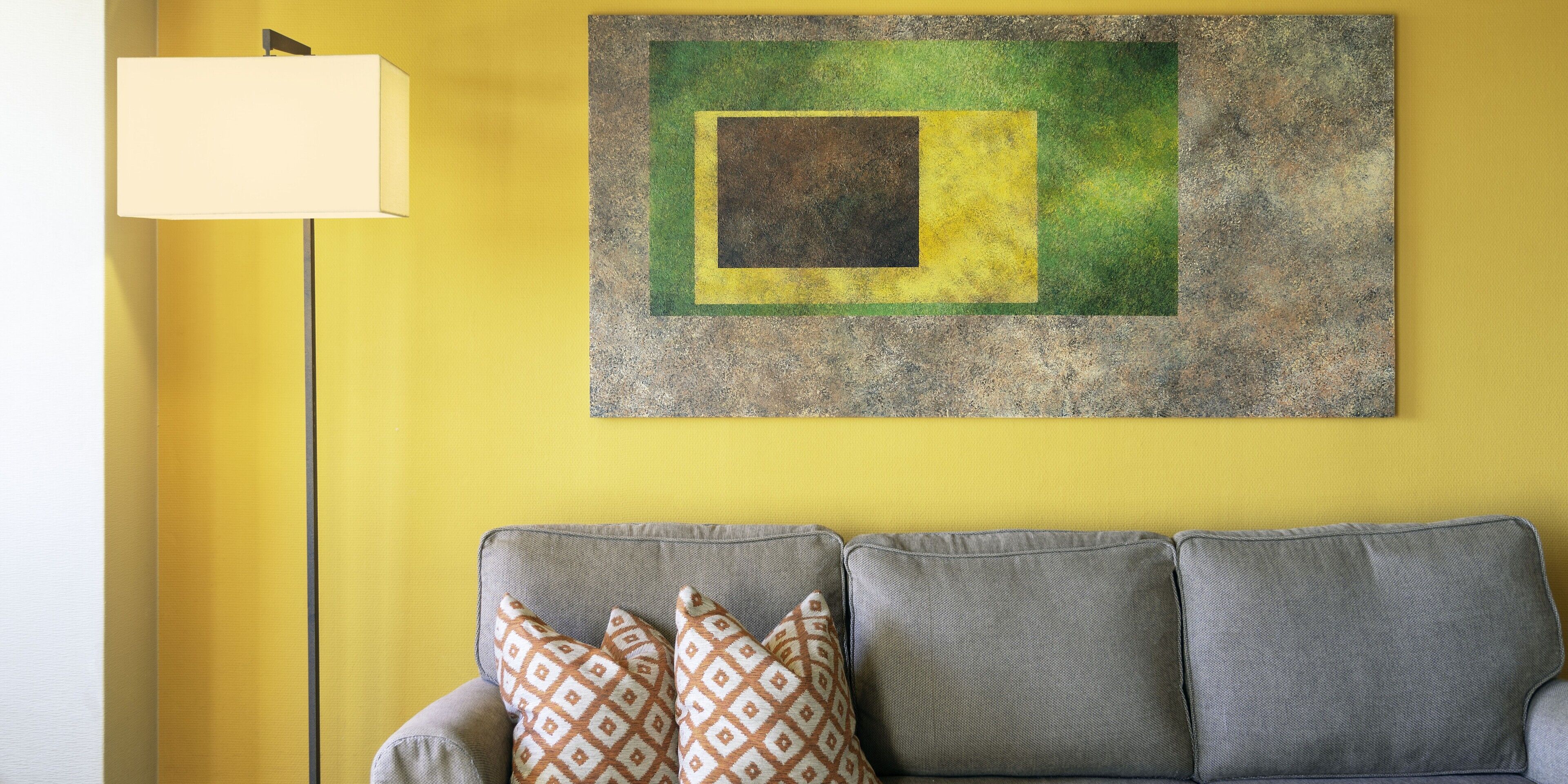 A living room with a yellow wall, a gray sofa with patterned cushions, and a framed abstract painting.