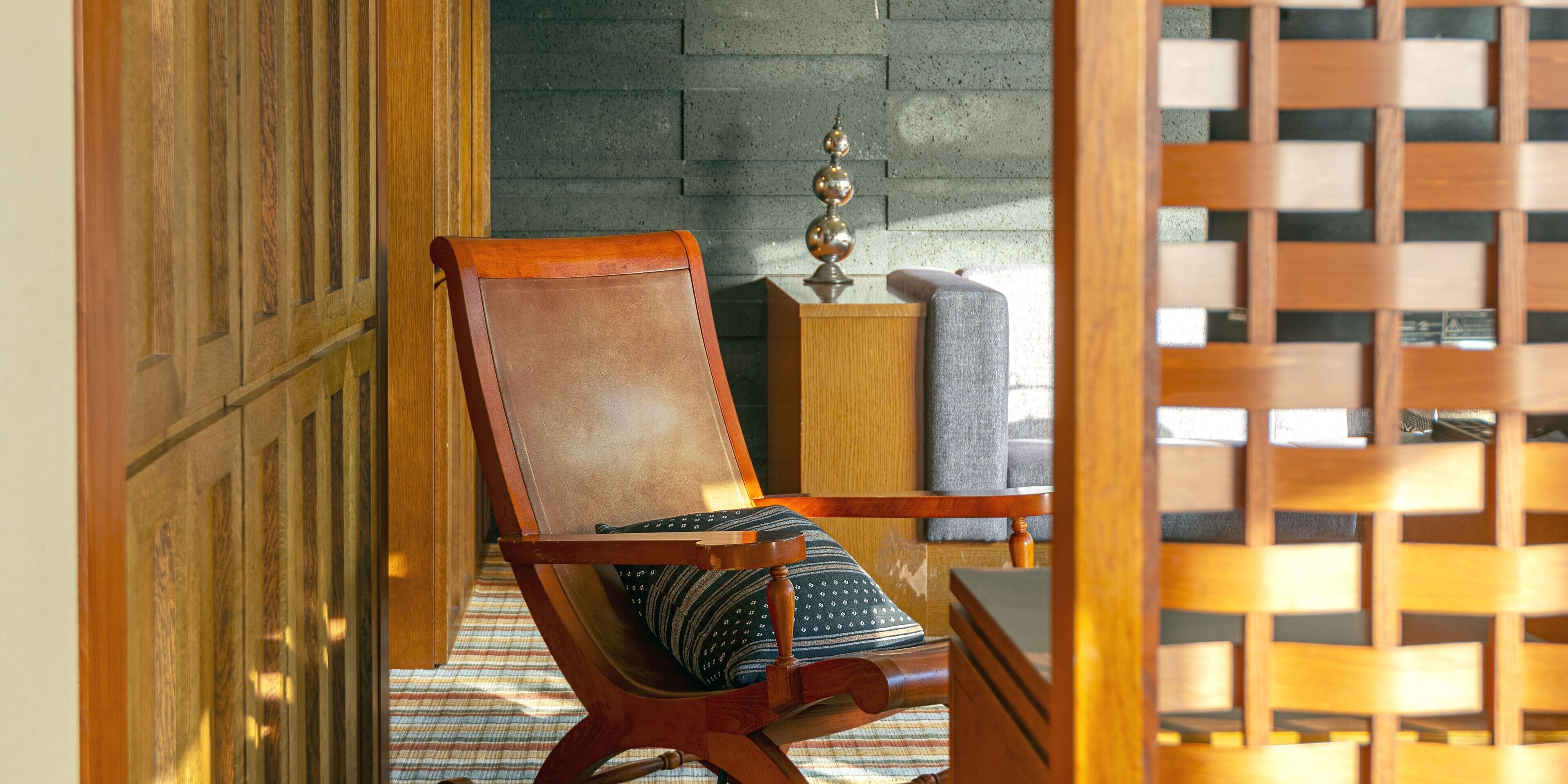 A wooden chair with a patterned cushion in a room with a concrete wall and a wooden lattice partition.