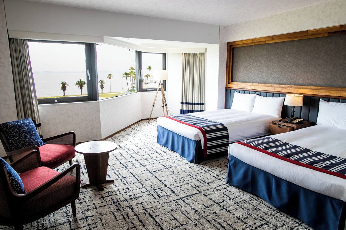 A hotel room with a large bed, a chair, a small table, and a view of the ocean.
