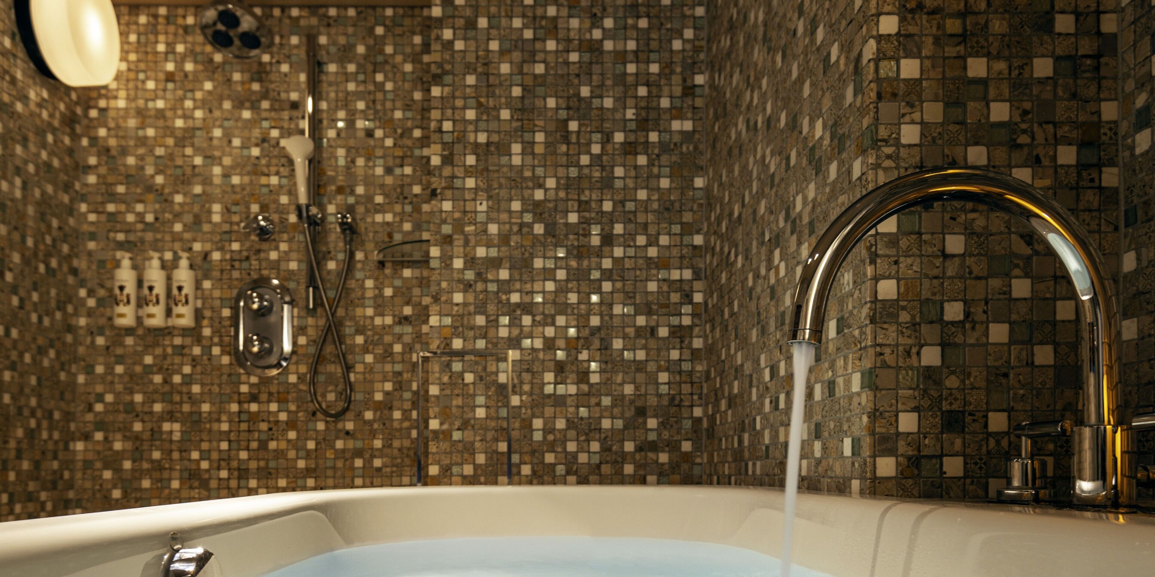 A bathroom with a mosaic tile wall, a bathtub, and a showerhead.