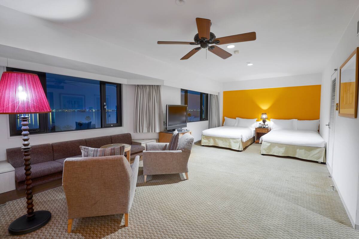 A hotel room with a bed, two armchairs, a sofa, a TV, and a large window with curtains.