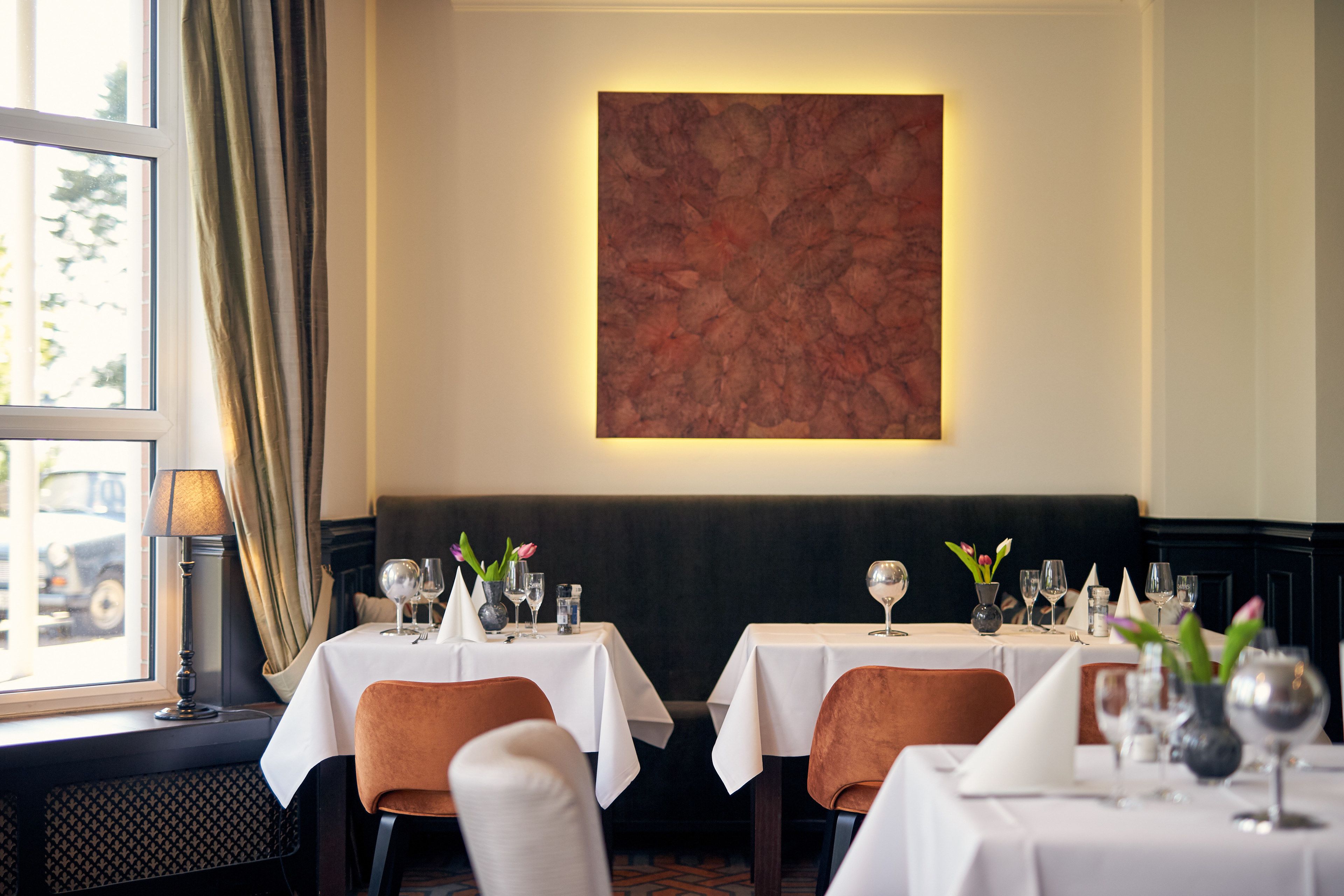 A restaurant with two tables, each with white tablecloths, chairs, and glassware.