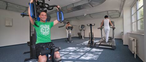 A gym with exercise equipment, a blue carpet, and large windows allowing natural light.