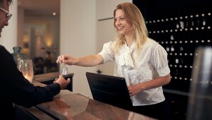 A person handing over a key to another person at a reception desk in a modern building.