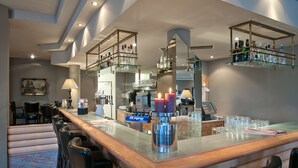 A bar area with a wooden counter, bar stools, and shelves with bottles.