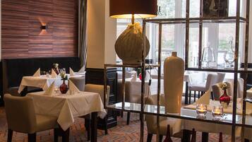 Un restaurante con varias mesas y sillas, un candelabro y vistas al exterior a través de amplias ventanas.