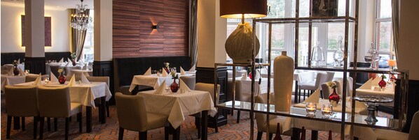 Un restaurante con varias mesas y sillas, un candelabro y vistas al exterior a través de amplias ventanas.