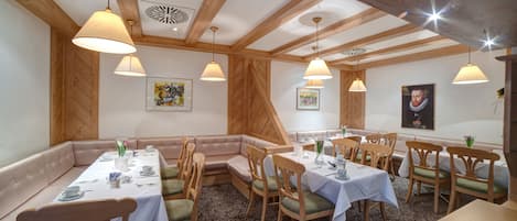 A dining area with wooden beams, white tables, and green cushioned seating.