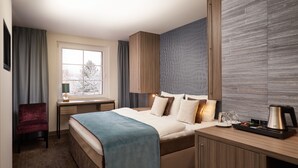 A hotel room with a bed, a desk, a chair, a coffee maker, and a window with a view of trees.