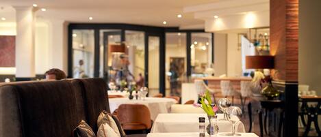 A restaurant with tables set for dining, a bar area, and a seating area with couches.