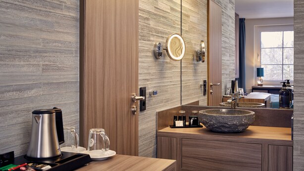 A modern bathroom with a stone sink, wooden cabinets, a large mirror, and a coffee maker.