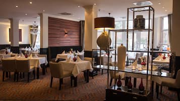 A restaurant with tables set for dining, a chandelier, and a decorative glass shelf.