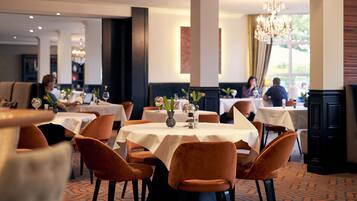 A restaurant with round tables, orange chairs, and a chandelier.