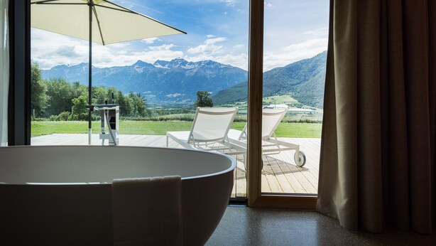 A modern bathroom with a large bathtub, a white chair, and an umbrella. - Hotel Garberhof (Malles Venosta)