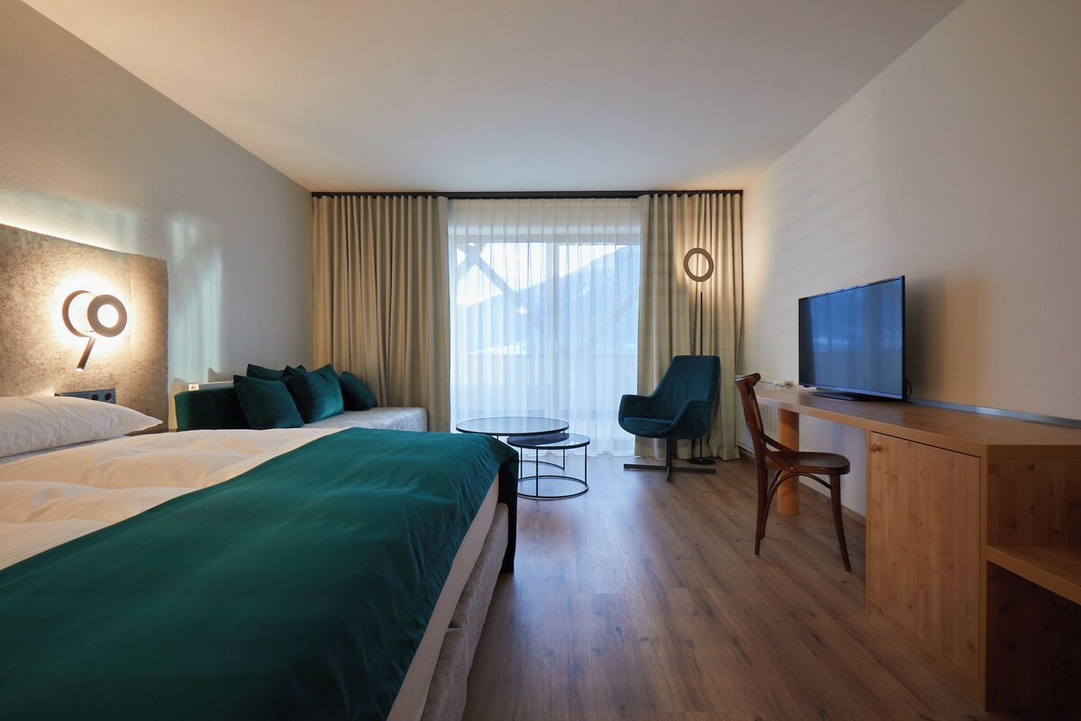 Een hotelkamer met een bed, een bureau, een stoel, een televisie en een raam met gordijnen.