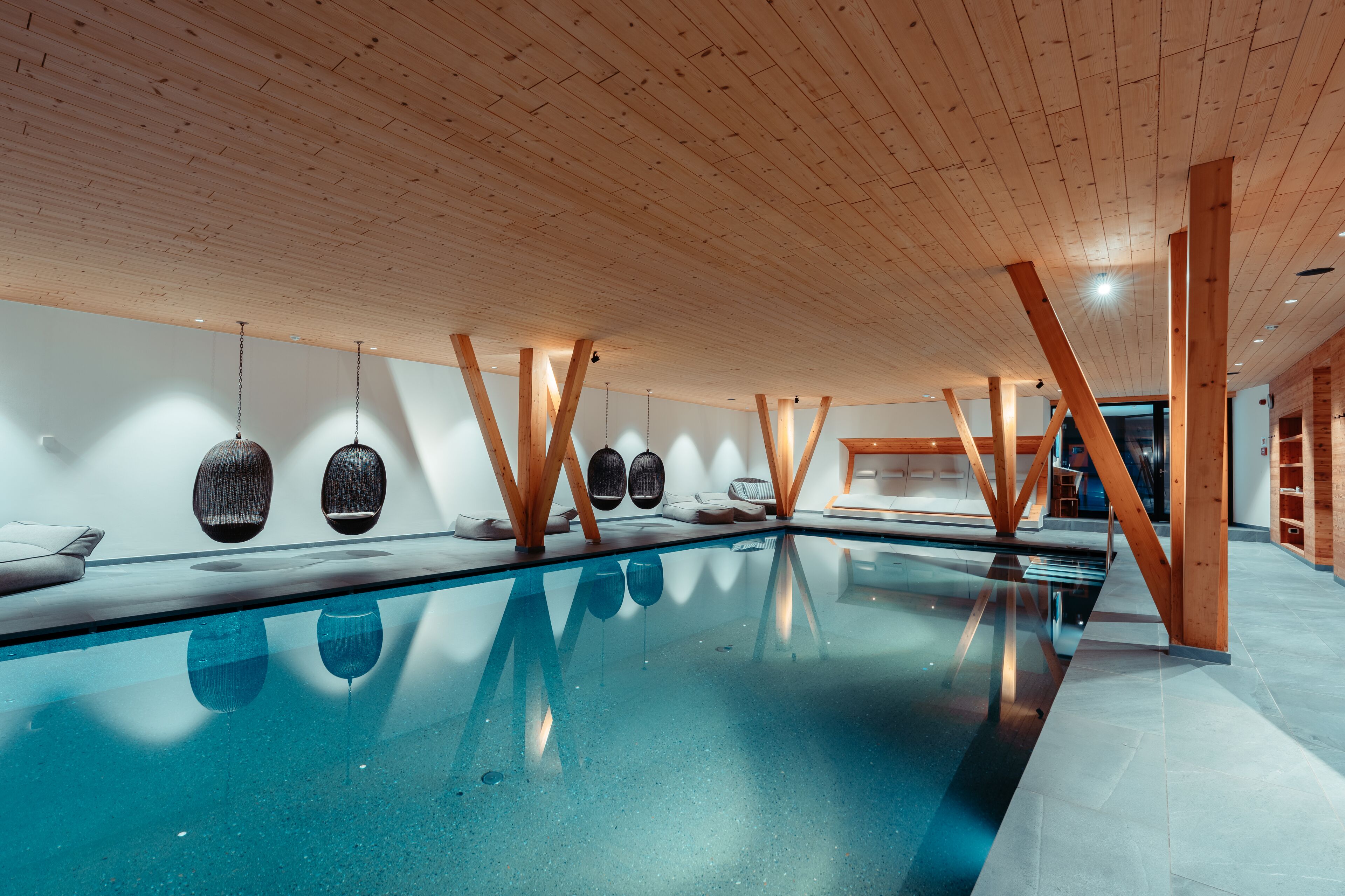 A modern indoor swimming pool with wooden beams and hanging light fixtures.