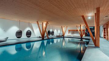 A modern indoor swimming pool with wooden beams and hanging light fixtures.