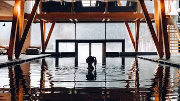 A large indoor swimming pool with wooden beams and a view of a snowy landscape through large windows.
