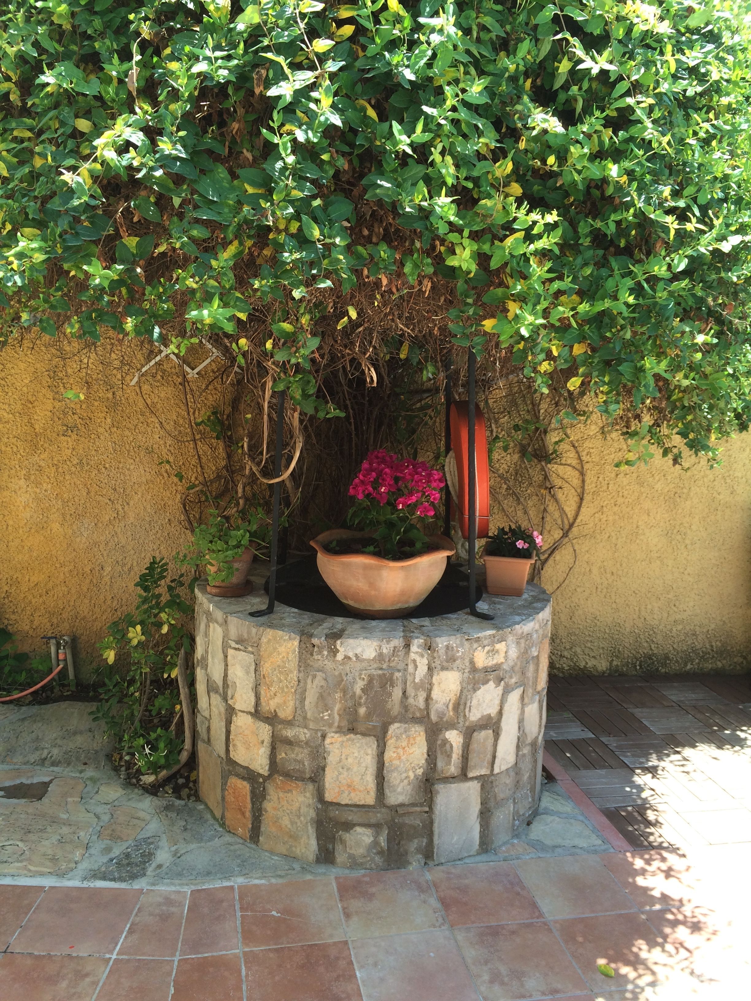 Una jardinera de piedra con plantas y flores en macetas frente a una pared con textura.