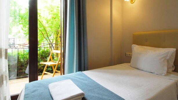 Habitación de hotel con cama, una silla, ventana con cortinas y balcón.