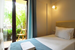 A hotel room with a bed, a chair, a window with curtains, and a balcony.