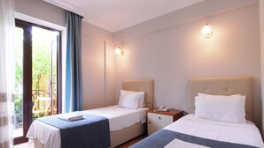 Una habitación de hotel con dos camas, una mesita, una lámpara de noche y un ventanal con cortinas.