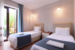 A hotel room with two beds, a small table, a nightstand, and a window with curtains.