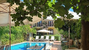 Zona de piscina con sillones de descanso, una piscina y un área de estar cubierta con sombrillas.