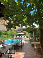 A poolside area with lounge chairs, a pool, and a covered seating area with umbrellas.