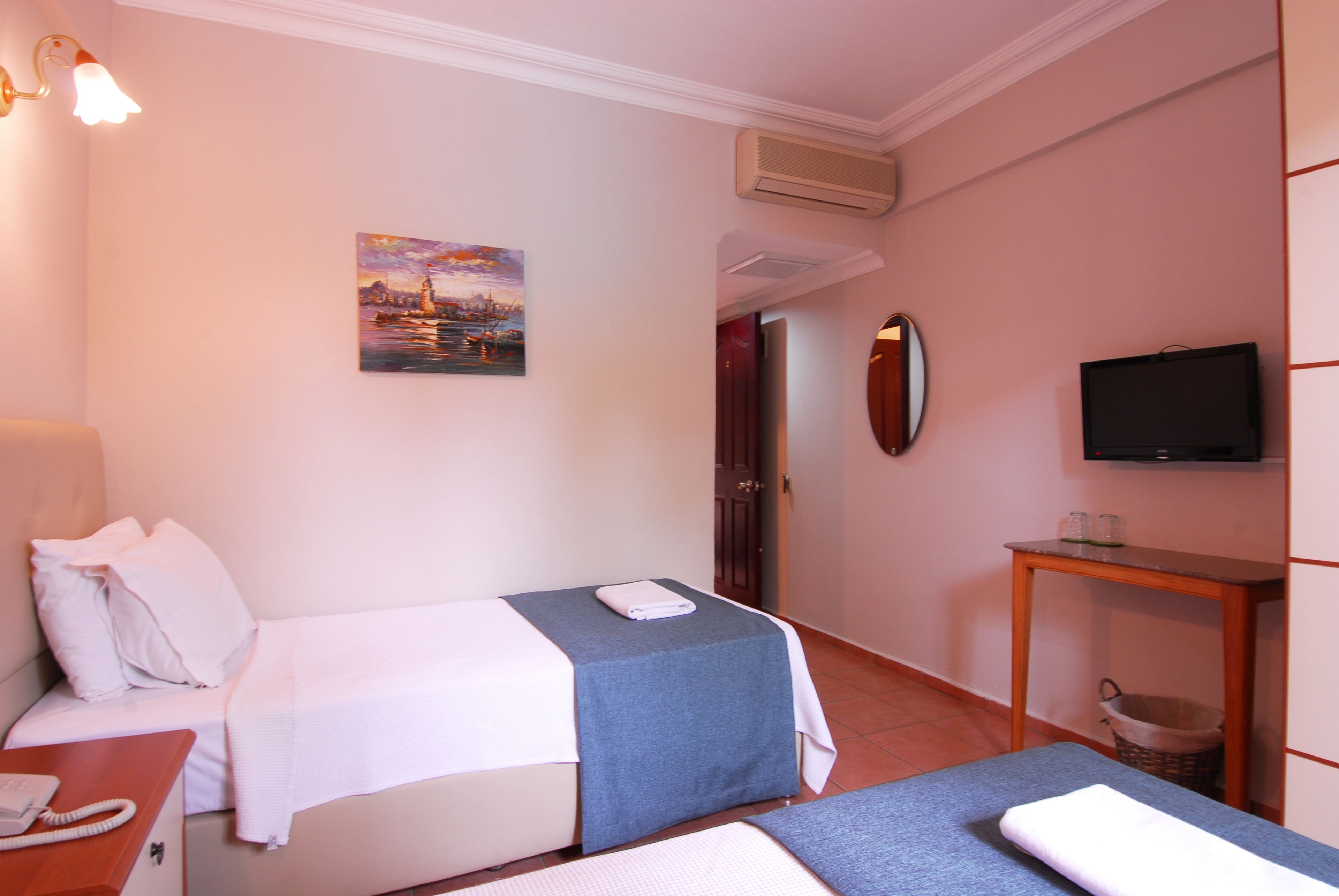 A hotel room with two beds, a television, a painting, and a small table with a telephone.