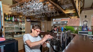 Zona de bar con un bartender preparando bebidas, estantes con botellas y vasos, y un techo de madera con luces colgantes.