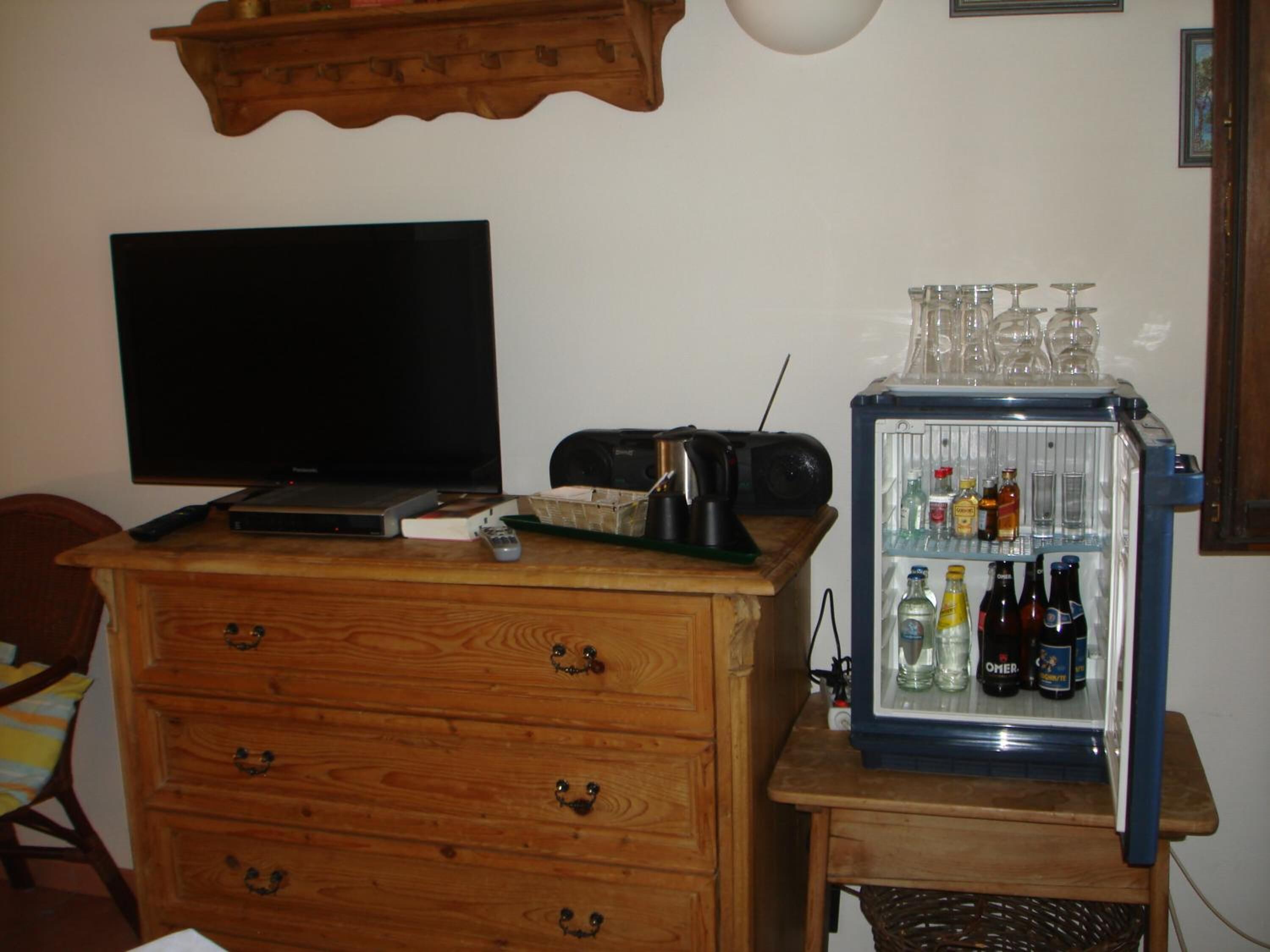 Une chambre dotée d’une commode en bois, d’un téléviseur et d’un mini-réfrigérateur rempli de boissons.