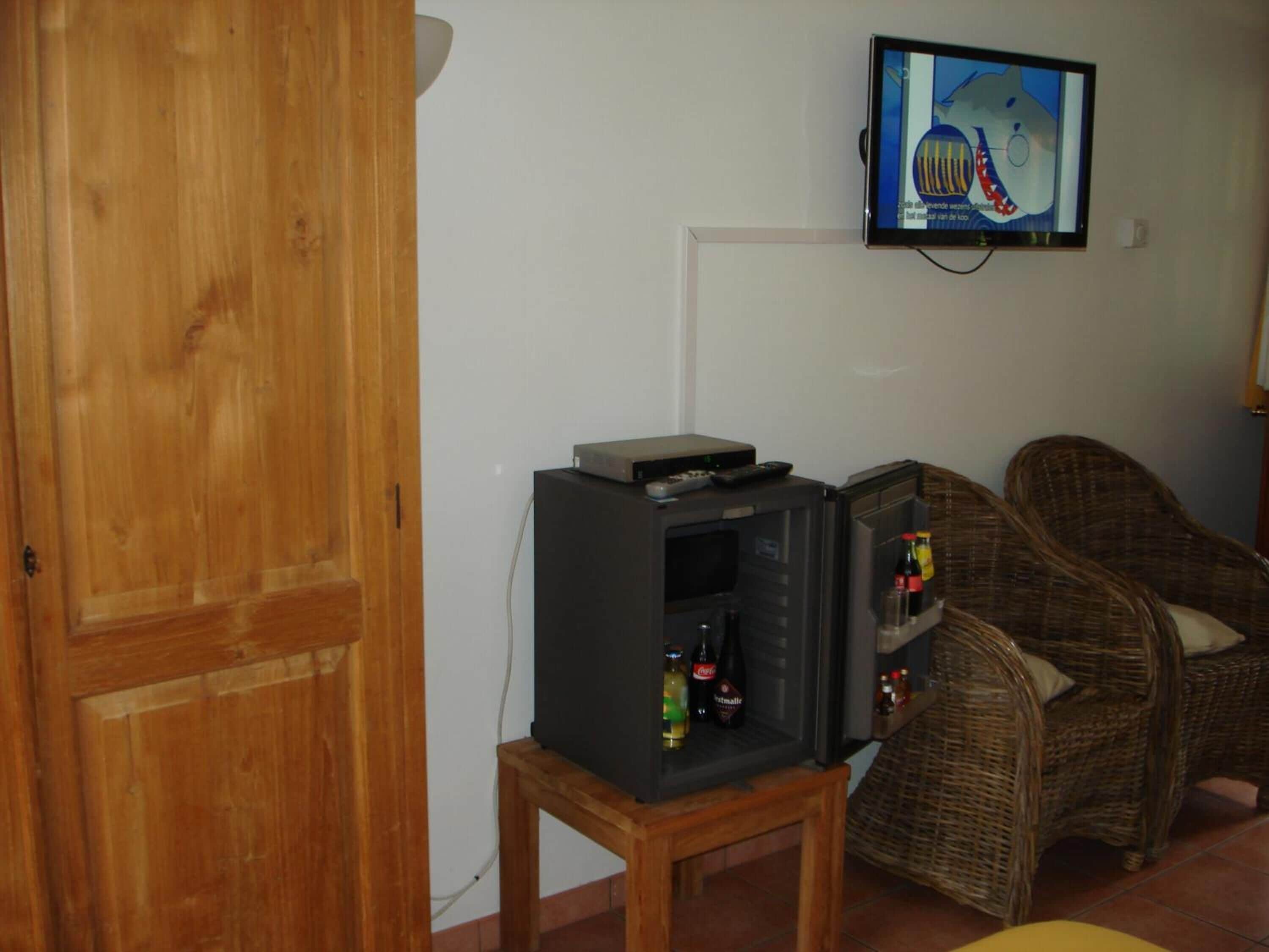 Una sala de estar con televisor montado en la pared, una mesita con reproductor de DVD y muebles de mimbre.