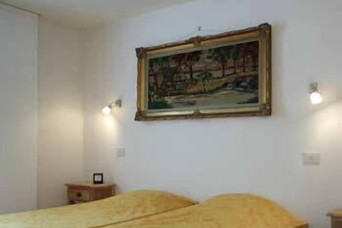 A bedroom with two beds, a painting on the wall, and bedside lamps.