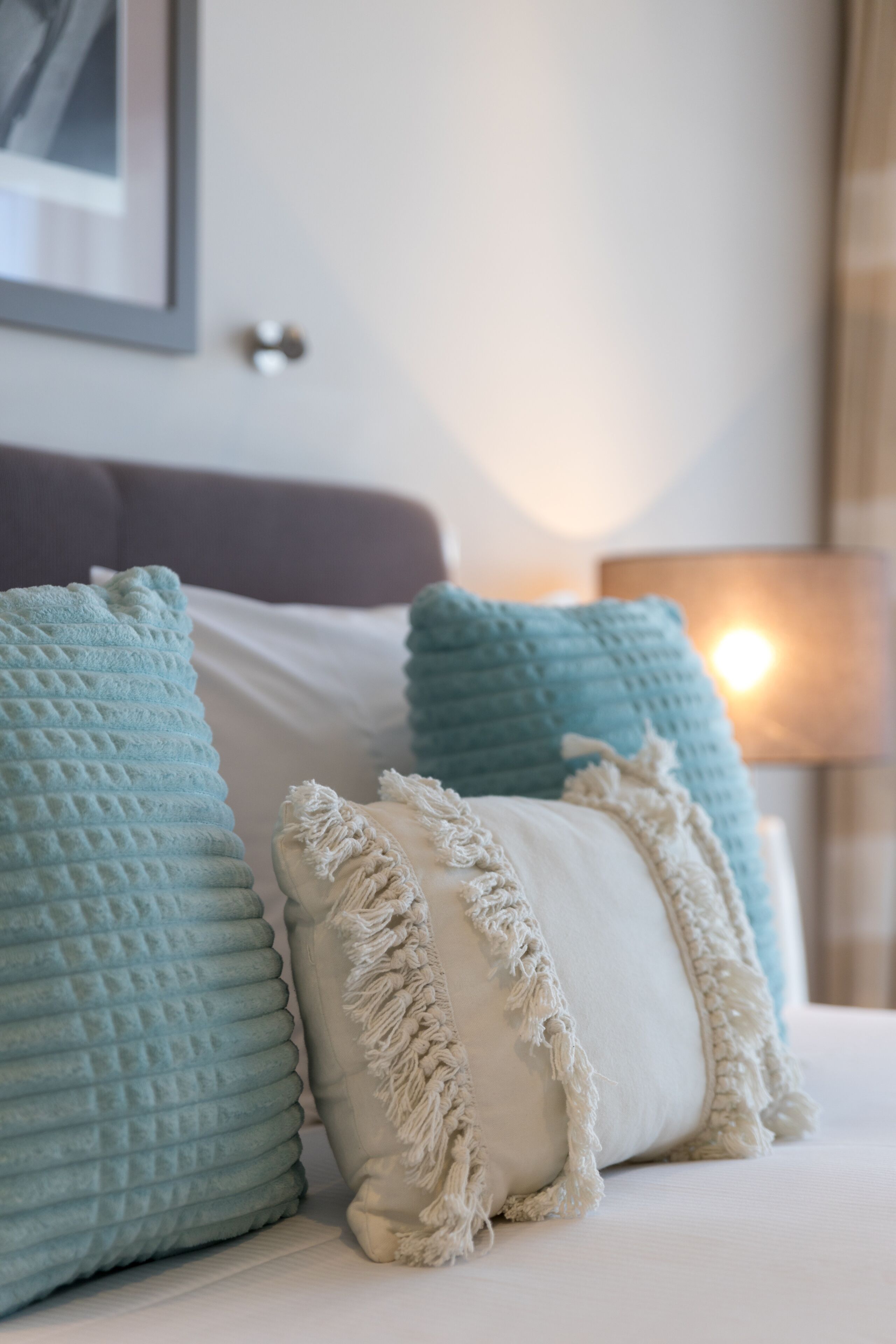 A neatly made bed with a white comforter and two pillows, one with a textured pattern and the other with a fringe detail.