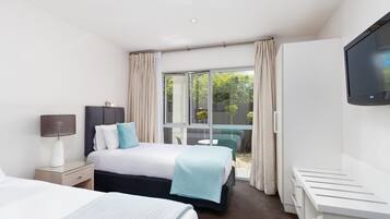 Quarto de hotel com uma cama, uma mesa de cabeceira com abajur, uma televisão na parede e uma porta de vidro deslizante para o exterior.