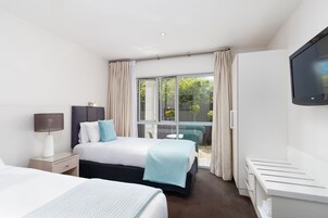 A hotel room with a bed, a bedside table with a lamp, a TV mounted on the wall, and a sliding glass door to the outside.