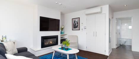A modern living room with a sofa, a coffee table, a fireplace, and a TV mounted on the wall.