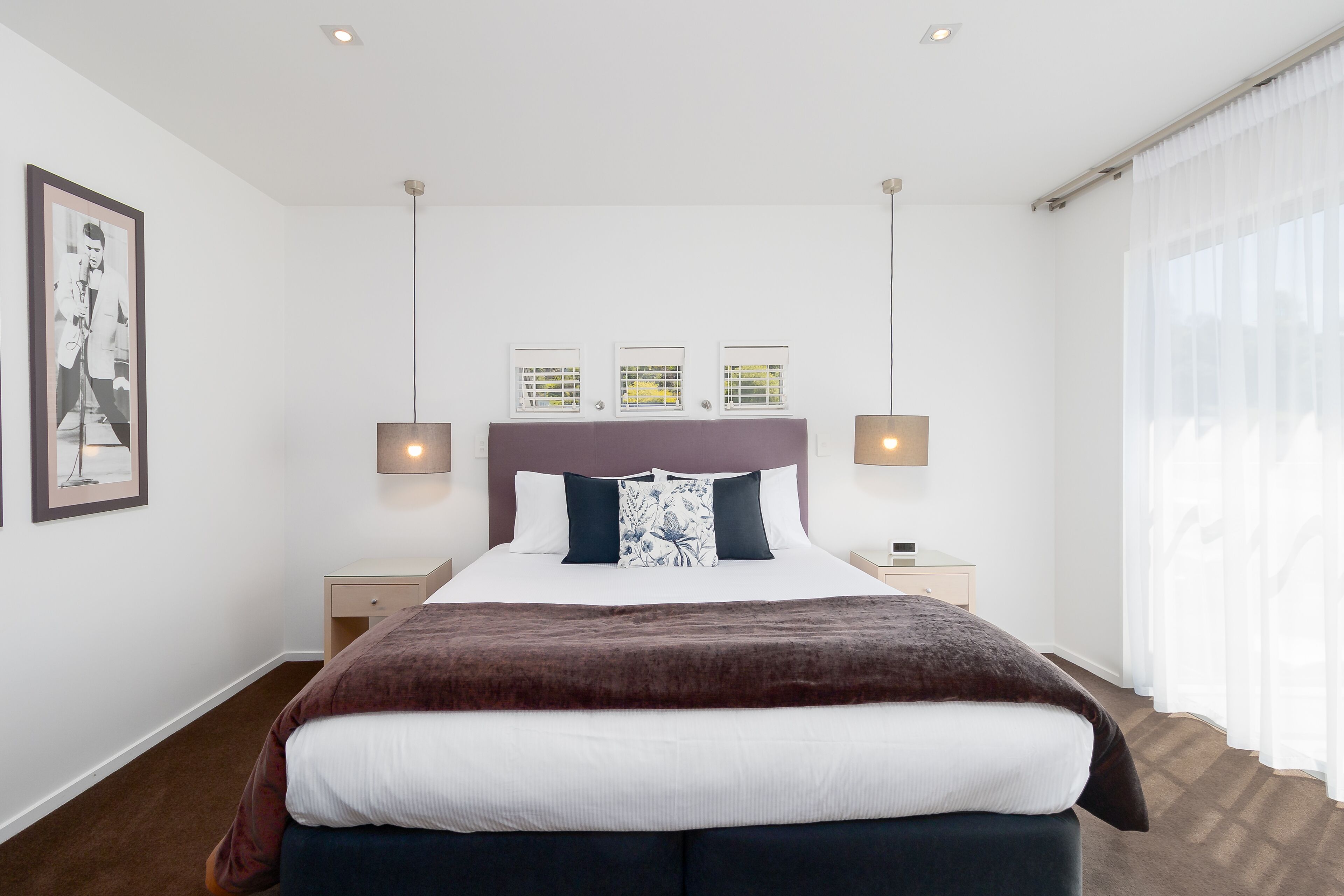 Une chambre à coucher bien aménagée, avec un grand lit, deux tables de chevet et une tête de lit ornée de trois petites fenêtres.