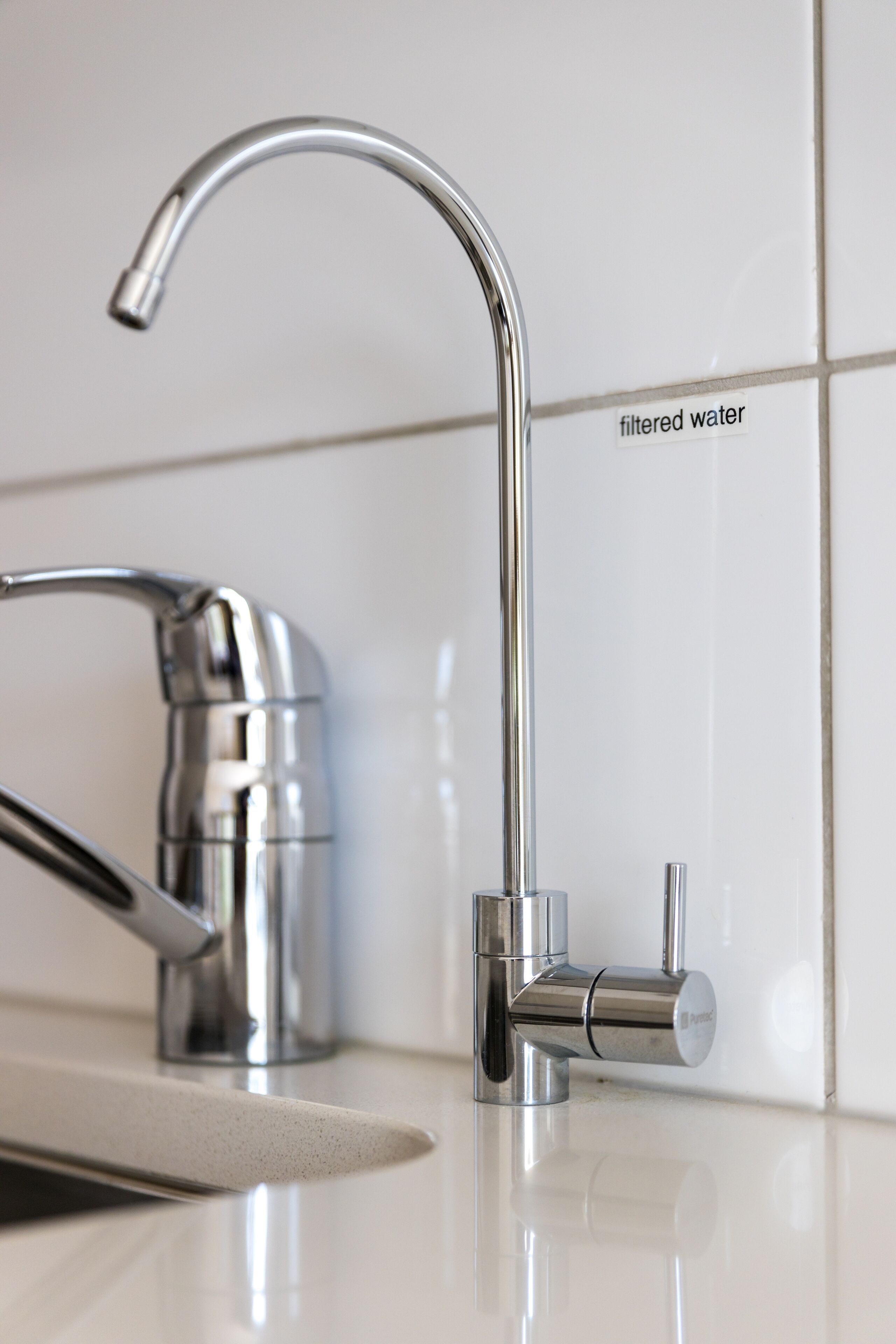 A modern kitchen faucet with a pull-down spray head and a separate hot water tap.